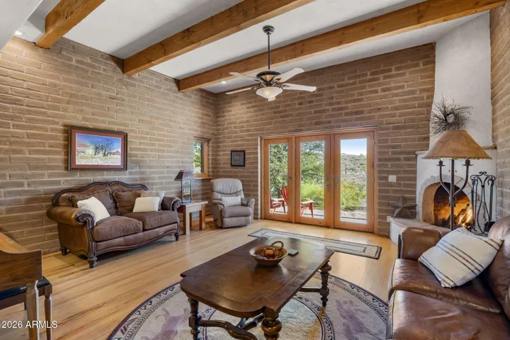 Comfortable living area featuring exposed wood beams, hardwood flooring, a corner fireplace, and French doors leading outdoors.