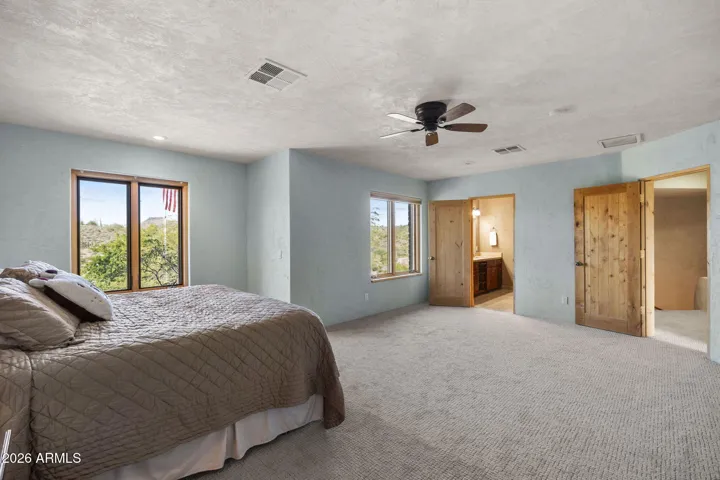Generously sized primary suite with multiple windows, ceiling fan, and ample space for a sitting area.