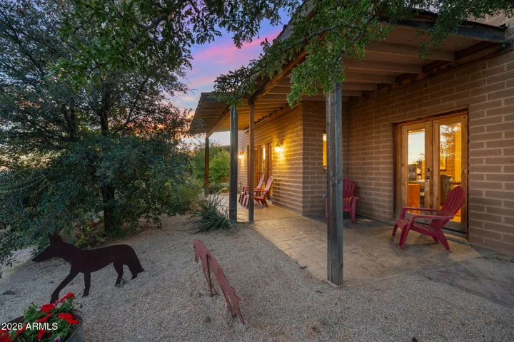 Extended covered patio with exposed wood beams and ambient lighting, offering comfortable outdoor seating and direct access to the backyard.
