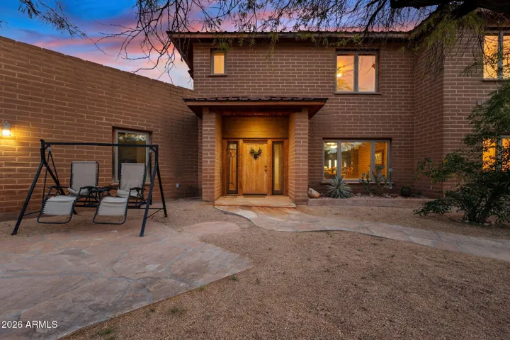 Inviting front courtyard with brick façade, warm exterior lighting, and custom wood entry door creating a welcoming evening ambiance.