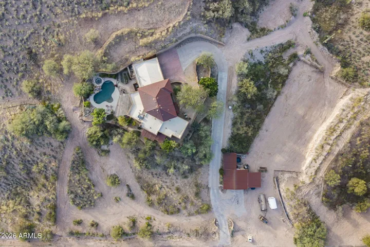 Overhead aerial perspective showcasing the home’s footprint, circular driveway, detached garage structure, and expansive desert setting.