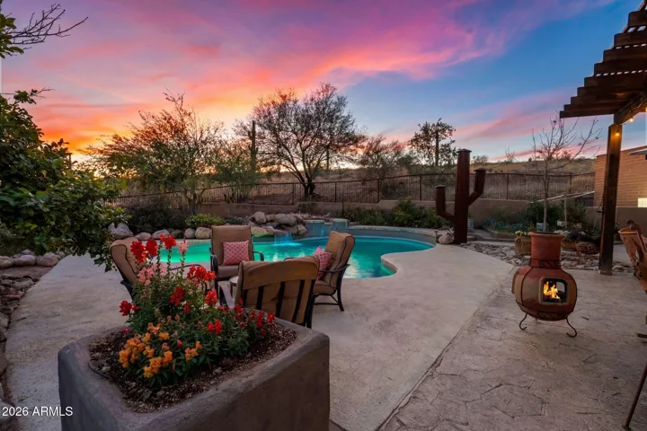 Resort-style pool illuminated at sunset with raised spa, natural stone accents, and nearby chiminea for cozy evening gatherings.