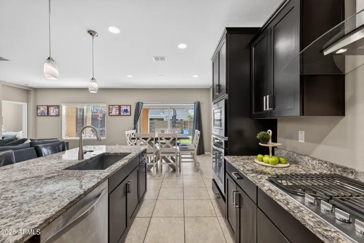 Gourmet Eat-in Kitchen Showcases 42" Expresso Staggered Cabinets with Pullouts, Granite Counters, Recessed lighting, Walk-In Pantry, Pendant Lights, Canopy Hood, Wall Oven/Microwave, 5 Burner Gas Cooktop, Single Bowl Sink, and a Center Island with Breakfast Bar.