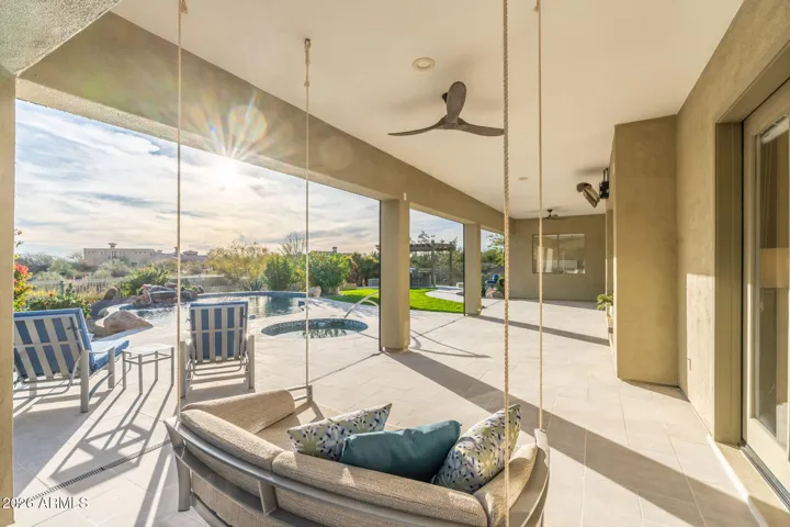 Spacious Scottsdale covered patio featuring stylish swing seating, ceiling fans, and views of the pool and backyard retreat.