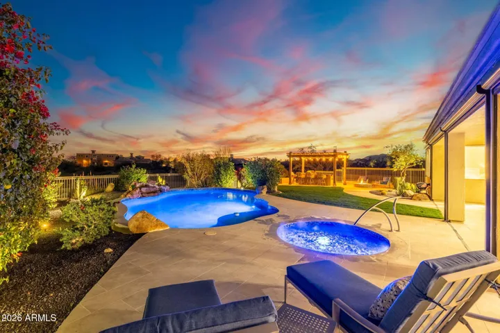 Resort-style Scottsdale backyard featuring a glowing pool, spa, desert landscaping, and pergola entertaining space under a vibrant sunset sky.