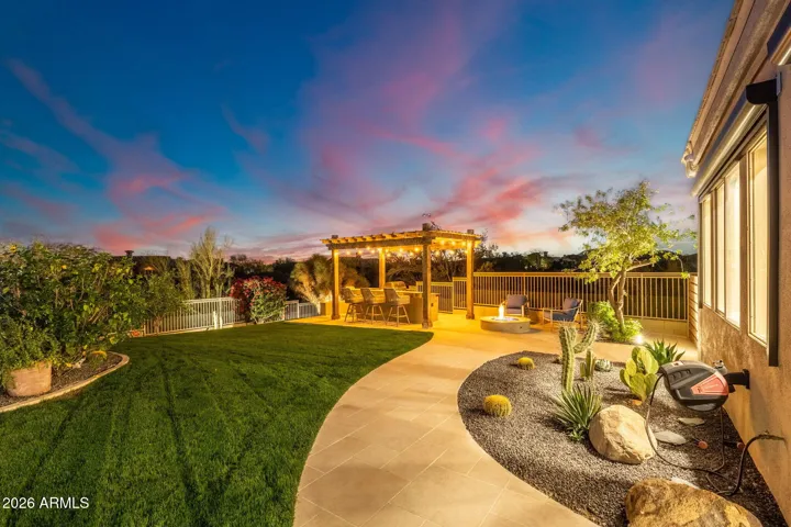 Beautifully landscaped backyard with manicured lawn, desert plants, and pergola entertaining area, offering peaceful Scottsdale outdoor living with sunset views.