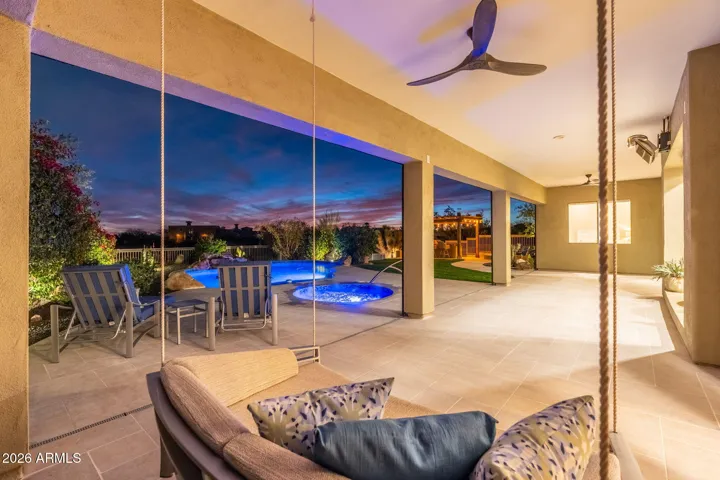 Covered patio with a stylish swing seat overlooking the illuminated pool and spa, offering a relaxing Scottsdale outdoor retreat with scenic evening views.