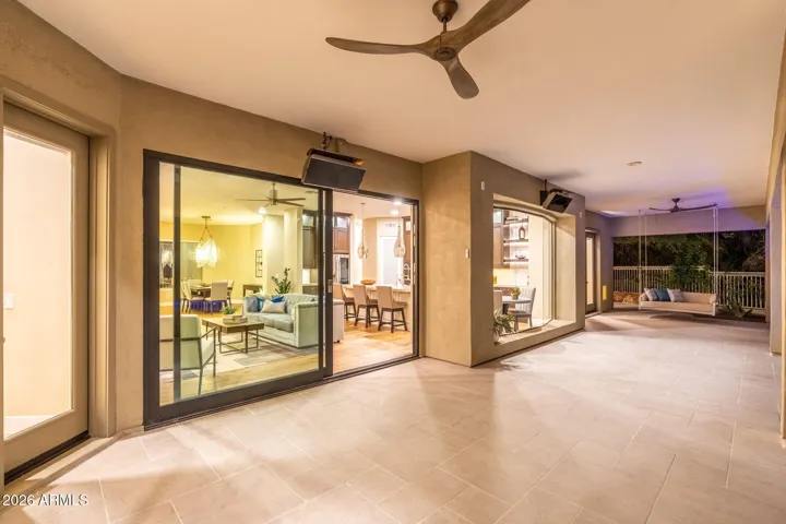 Spacious covered patio with modern tile flooring and ceiling fans, featuring large sliding glass doors that create seamless indoor-outdoor living in this Scottsdale home.