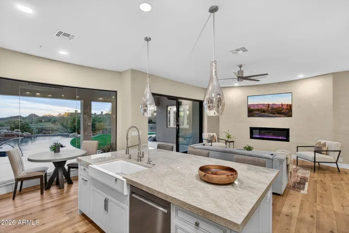 Bright Scottsdale kitchen with a large island, farmhouse sink, pendant lighting, and expansive windows overlooking the backyard pool and landscaping.
