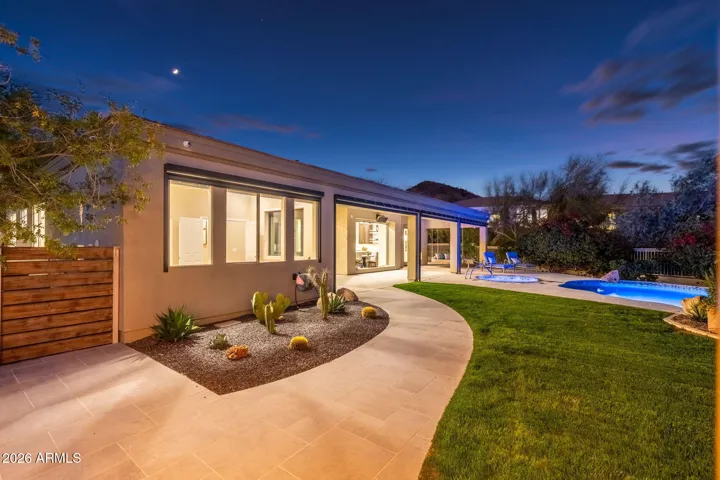 Spacious covered patio with seamless indoor-outdoor flow, overlooking a lush green lawn, pool, and professionally landscaped Scottsdale backyard.