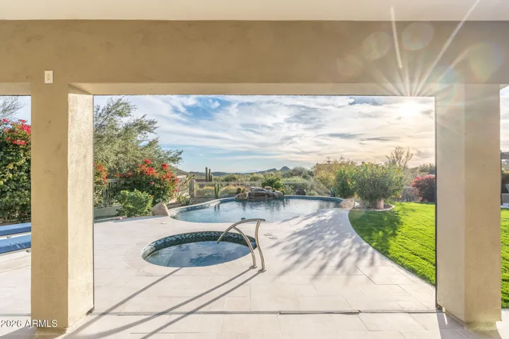 Scenic Scottsdale backyard view from covered patio showcasing pool, spa, and landscaped yard with mountain views and desert surroundings.