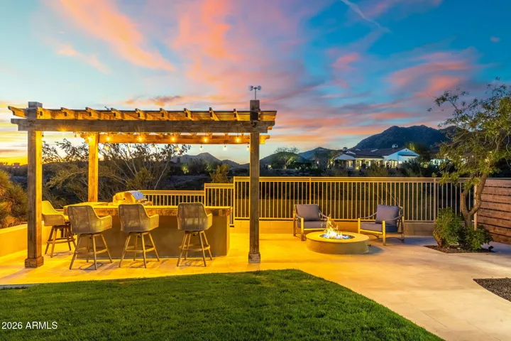 Inviting outdoor living space with pergola-covered kitchen, bar seating, and fire pit, offering scenic Scottsdale mountain views and premium entertaining space.