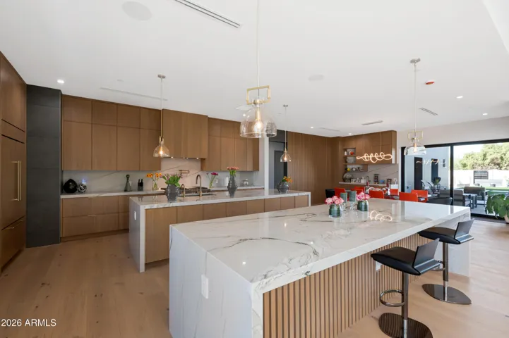 Stunning open kitchen and dining area with oversized island, designer lighting, and seamless indoor-outdoor views. This Paradise Valley home offers luxury and functionality.