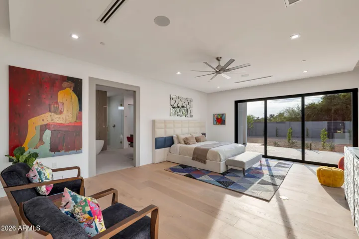 Spacious primary bedroom with wide plank wood flooring, modern ceiling fan, and expansive sliding glass doors opening to the backyard. This Paradise Valley luxury home offers natural light, indoor-outdoor living, and a peaceful retreat.