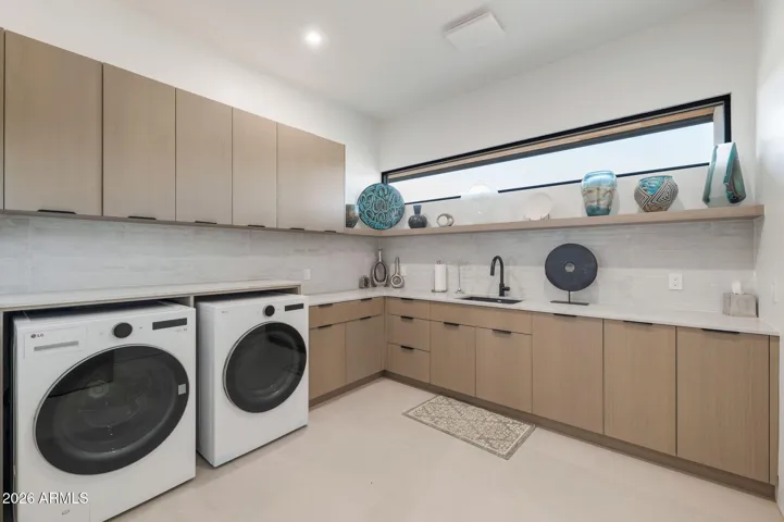 Bright and spacious laundry room featuring modern cabinetry, quartz countertops, and front-load washer and dryer. This Paradise Valley home includes functional design, ample storage, and updated finishes for everyday convenience.