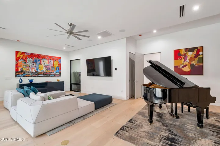 Sophisticated living room with wide plank flooring, contemporary art, built-in entertainment space, and a grand piano. This Paradise Valley home blends luxury design with comfortable everyday living.