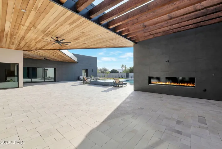 Expansive covered patio in Paradise Valley featuring wood ceiling details, a modern linear fireplace, and seamless views of the resort-style pool. Designed for indoor-outdoor living, this space is perfect for entertaining and relaxing year-round.