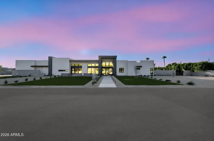 Stunning dusk exterior with warm interior lighting highlighting the modern architecture. This Paradise Valley home offers striking curb appeal and a sophisticated evening ambiance.