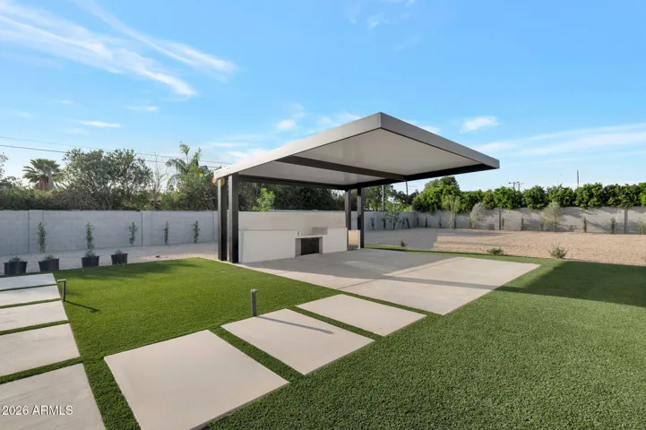 Stylish backyard with covered trellis, outdoor kitchen setup, and lush turf. This Paradise Valley home provides a perfect space for entertaining and outdoor dining.