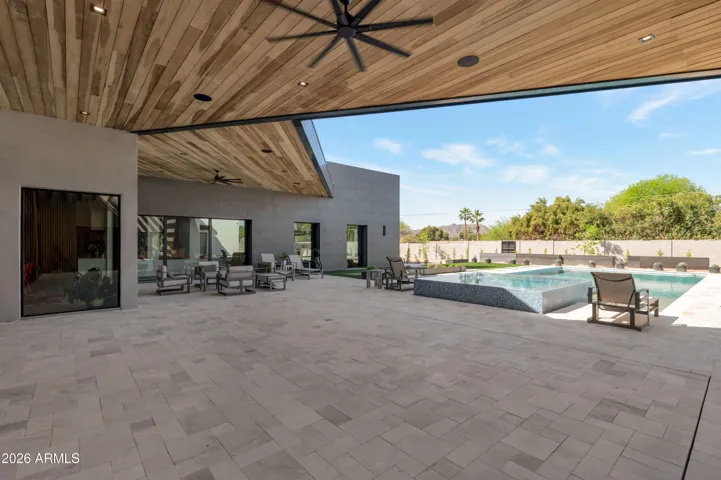 Expansive covered patio with wood ceiling detail and ceiling fans, overlooking the pool and backyard. This Paradise Valley home is designed for indoor-outdoor living and entertaining.