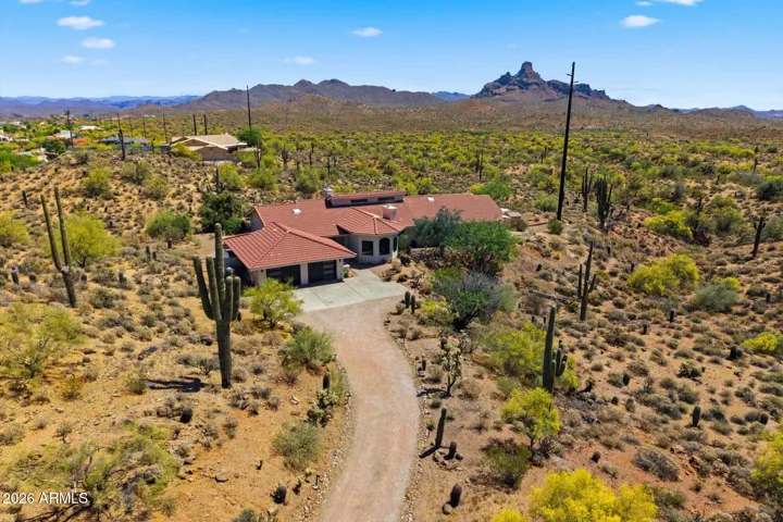 Expansive aerial view of the home nestled in the desert, showcasing the long driveway and surrounding mountain ranges.