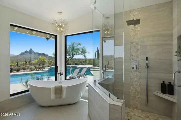 Luxurious primary bathroom featuring a freestanding tub, walk-in shower, and stunning views of the pool and desert landscape.