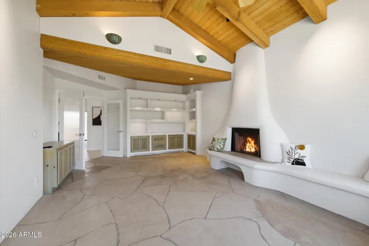 Versatile den featuring a unique fireplace, custom built-in shelving, and a stunning wood-beamed ceiling.