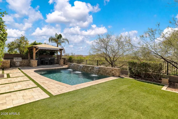 Private arroyo lot with no rear neighbors, featuring a Pebble Tec pool with cascading water features, travertine decking, turf, and a covered gazebo.