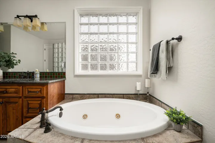 Inviting soaking tub set beneath a glass block window, creating a serene and private space for relaxation in this Phoenix primary suite.