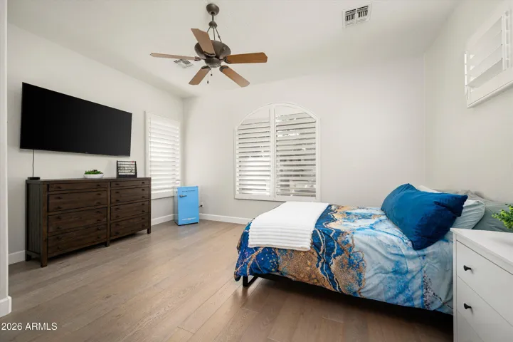 Spacious guest bedroom with plantation shutters, ceiling fan, and wood flooring, offering comfort and style in this Phoenix home.