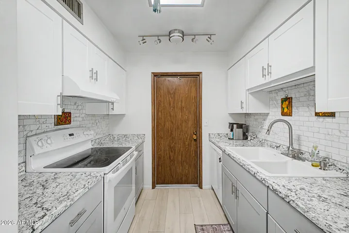 Remodeled shaker cabinets are light grey lowers and white uppers. White glass cooktop range, sink, dishwasher, skylight & fan.