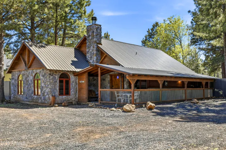 Charming stone and wood cabin with metal roof, covered front porch, and tall pines throughout the property