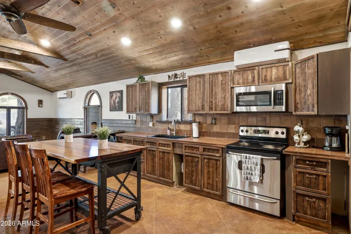 Rustic kitchen with wood cabinetry, tile backsplash, stainless steel appliances, and large island.