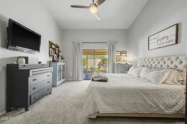 Light-filled bedroom featuring sliding glass doors leading to covered patio. Vaulted ceilings and neutral finishes create a relaxing space in this Peoria Property.