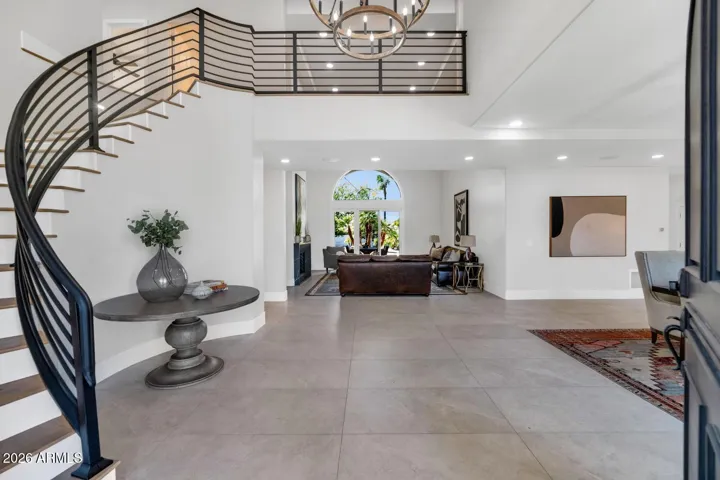 First impressions here are lasting ones. A sweeping curved staircase with custom iron railings rises through soaring double-height ceilings, drawing the eye upward to a statement chandelier that anchors the space with warmth and elegance. Large-format porcelain flooring flows underfoot, establishing the refined, cohesive design language that carries throughout every room of the home.