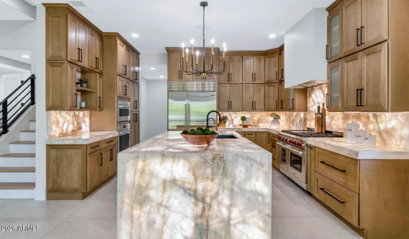 The full scale of this kitchen becomes apparent from this vantage point — generous counter runs, an oversized island, and cabinetry that extends to the ceiling on every wall. The warm alder tones and backlit Cristallo stone create a space that feels luxurious at any hour of the day.
