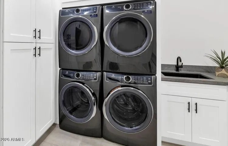 A well-appointed laundry room with stacked washer and dryer units included in the sale, white cabinetry for ample storage, and dedicated space for an additional refrigerator. Practical, polished, and exactly what it should be.