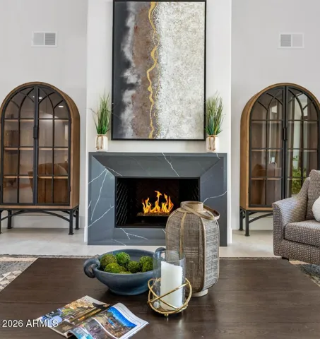 From this vantage point the full scale of the double-height living room comes into focus. A stone-surround fireplace anchors the space, flanked by dramatic arched cabinetry that draws the eye upward and adds architectural depth rarely seen outside of a fully custom home. Every finish feels considered; every detail intentional.