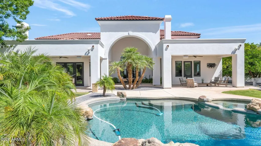 A wider perspective reveals the full scale of the property — the pool, the spa, the covered patios, and the home itself in one uninterrupted view. Nearly an acre of irrigated grounds, mature landscaping, and resort-caliber amenities, all within a private gated enclave.