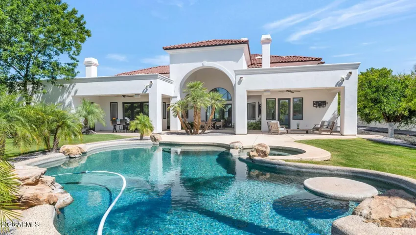 The resort-style pool and spa take center stage in this view, surrounded by lush, manicured grounds that belie the fact that this is an irrigated nearly-acre lot in the heart of the Valley. The Mediterranean-inspired arched covered patio anchors the rear elevation, creating an outdoor living environment that is as considered as anything found inside.