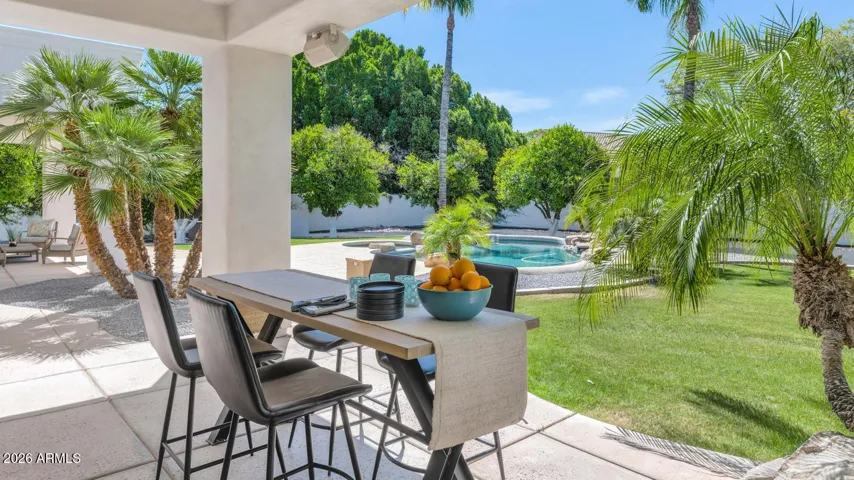 An elegant outdoor dining setup nestled beneath the covered patio invites alfresco meals in the shade of the home's signature arched architecture. The seamless flow between the great room and this outdoor space makes entertaining feel entirely effortless — indoors and out become one.