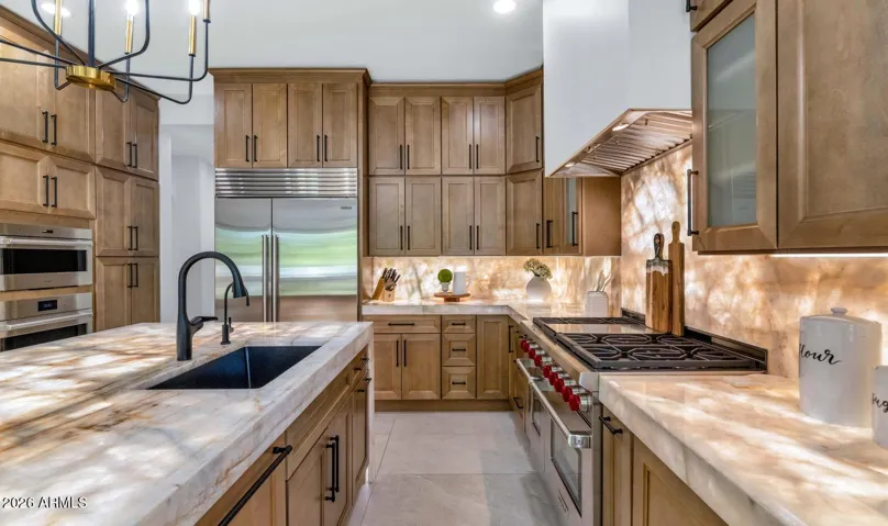 Every element of this kitchen was selected with intention. The Wolf professional range anchors the cooking wall, flanked by custom cabinetry and a richly veined Cristallo stone backsplash that glows with backlit warmth. A Cove dishwasher and Scotsman ice maker round out an appliance suite that would satisfy the most discerning home chef. Large-format porcelain flooring completes the space with quiet, enduring sophistication.