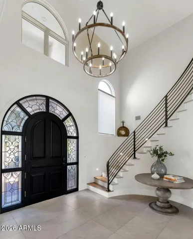 A second perspective of the foyer reveals the interplay of light, scale, and material that makes this entry so compelling. The curved staircase, custom iron railings, and chandelier above combine to create an arrival experience worthy of the home it introduces.