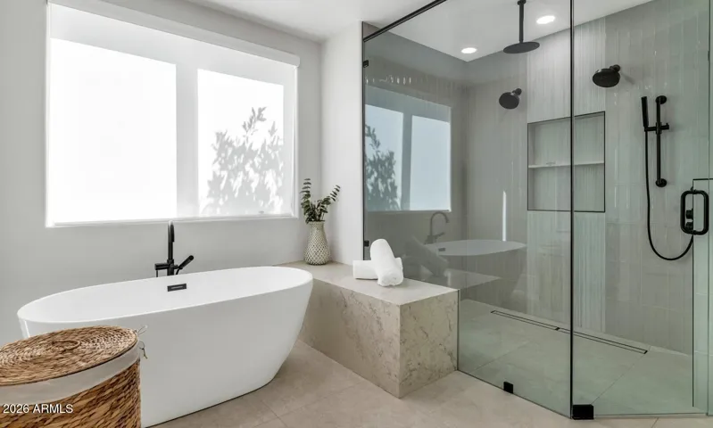 A freestanding soaking tub and frameless walk-in glass shower anchor opposite ends of this beautifully appointed bath. Clean lines, matte black fixtures, and a serene neutral surround create a space that would be equally at home in a five-star resort.