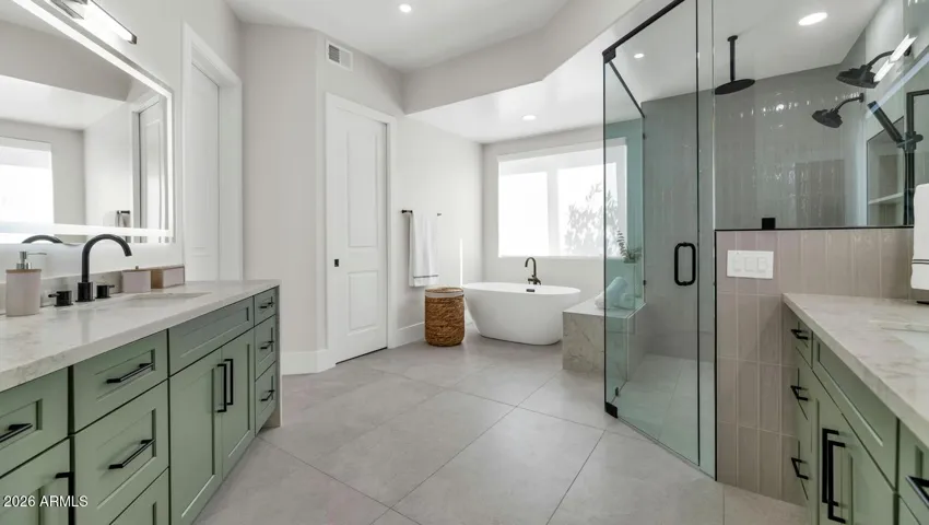 The full scope of the primary bath comes into view here — dual vanities, a freestanding soaking tub, and a walk-in glass shower, all finished in a cohesive palette of sage, white, and matte black. This is the bathroom buyers close their eyes and imagine at the end of a long day.