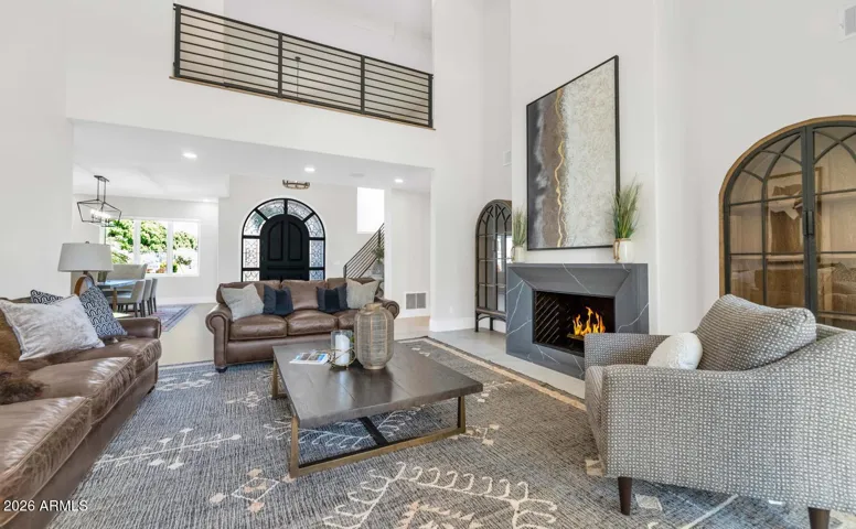 Gather around a beautifully appointed fireplace framed by the room's soaring double-height ceilings — the kind of space that feels equally suited to a quiet evening in or a lively dinner party that spills naturally from room to room. The warm, neutral palette and thoughtful material selections create a cohesion rarely found outside of a custom build.