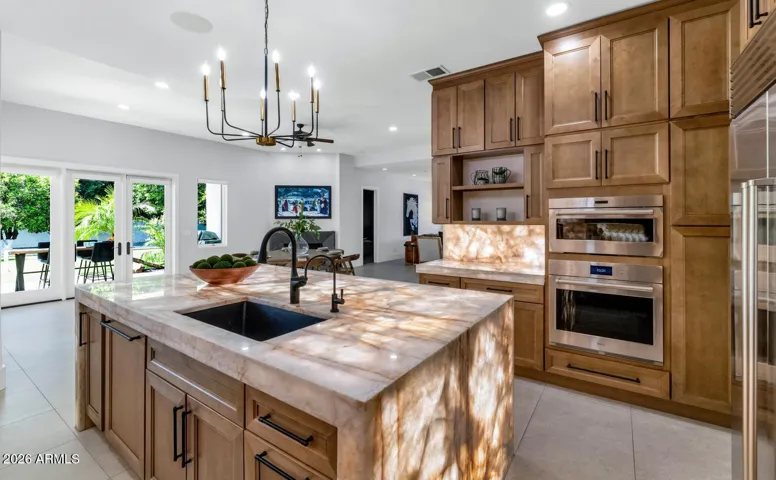 Natural light washes across the island from a well-positioned window, illuminating the Cristallo surface and reinforcing the kitchen's warm, welcoming energy. The island sink adds everyday functionality without interrupting the clean lines of the design — a thoughtful detail in a kitchen full of them.