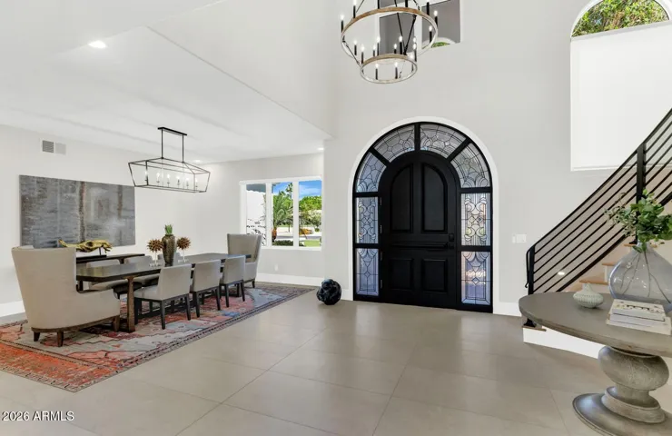 A second perspective of the entry reveals the full drama of the arched iron-and-glass front door and the cascading light from the chandelier above. Large-format porcelain flooring anchors the space, establishing the tone of intentional design that carries through every room of the home.