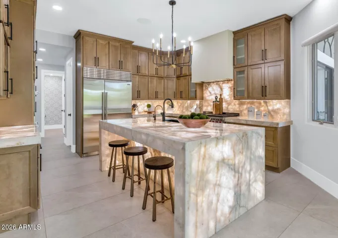 The kitchen is as functional as it is beautiful, designed for serious cooking and effortless hosting alike. Floor-to-ceiling cabinetry in a warm, lightly grained alder tone with matte black hardware provides exceptional storage while lending the space a grounded, custom feel. Large-format porcelain flooring continues seamlessly underfoot, unifying the open layout with quiet elegance.