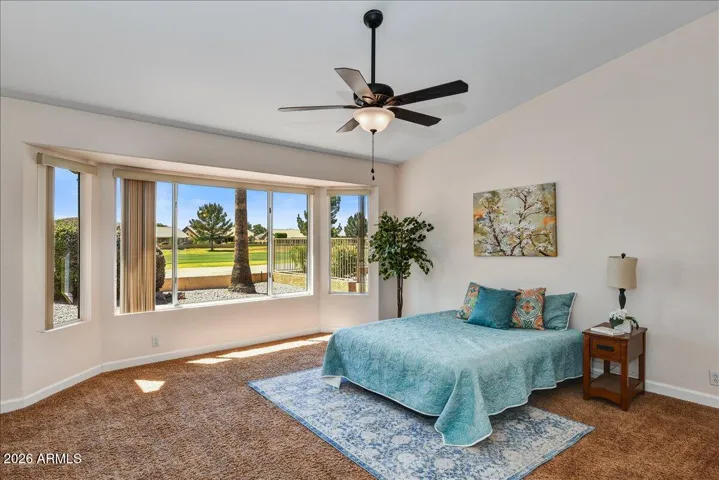 Retreat to the generous primary suite, featuring bay window, plush carpeting, a ceiling fan, and direct views of the golf course.